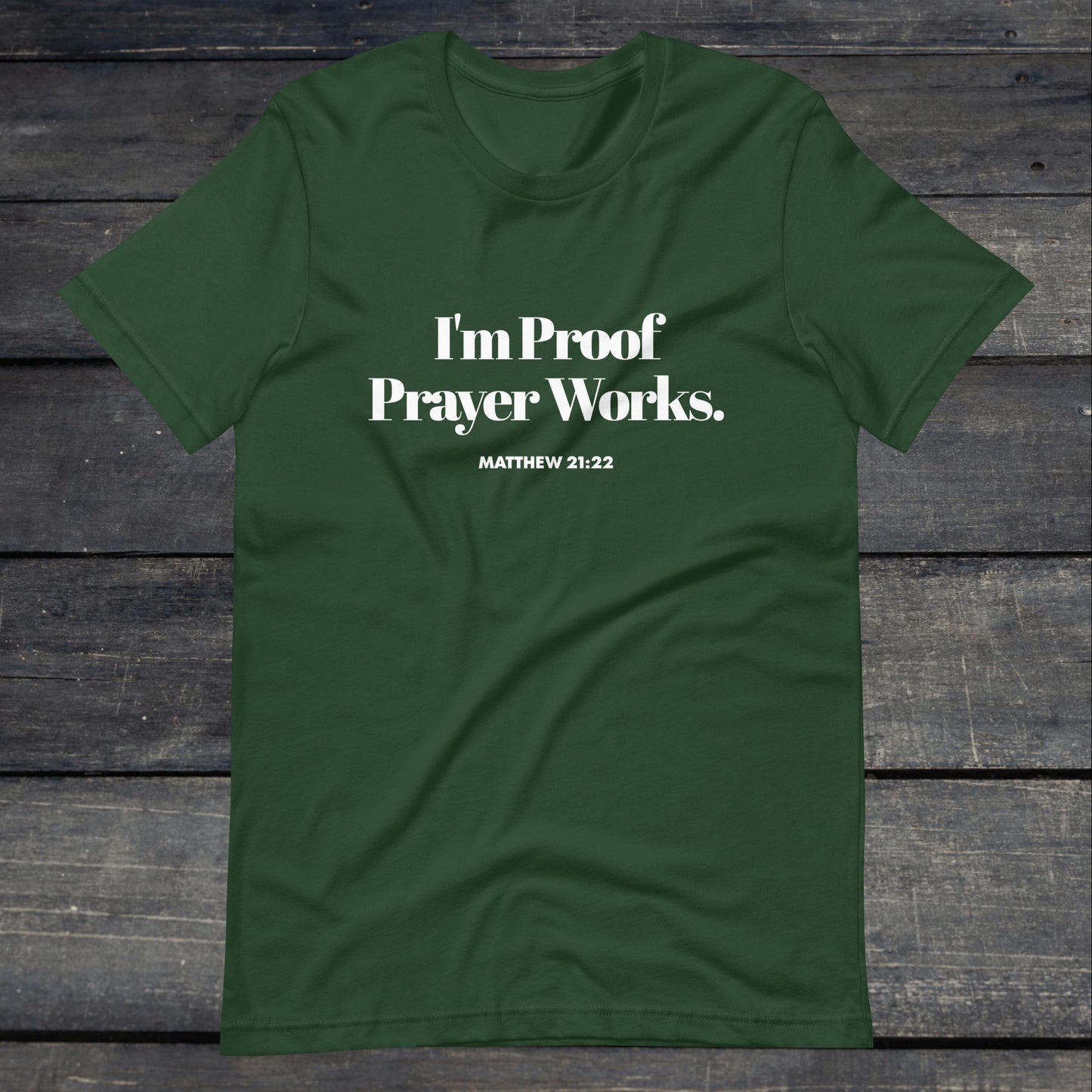 A photo of the "I'm proof prayer works" tee. The shirt color is forest green with white text that reads "I'm proof prayer works".