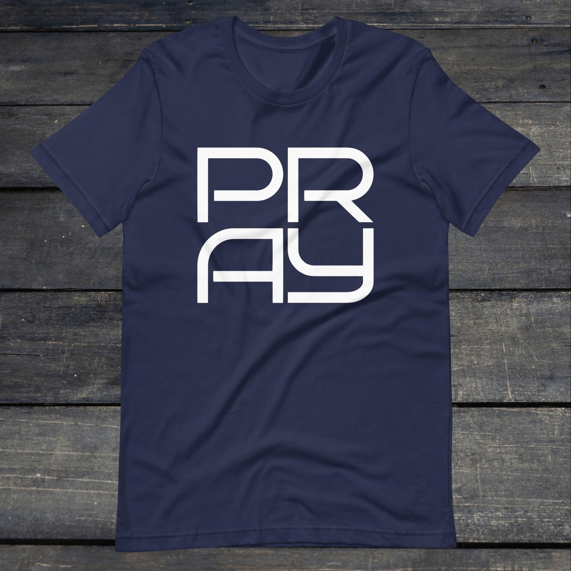 A photo of the Pray 4 Tee. This tee is navy blue with white text that reads P-R-A-Y in large stylish lettering.