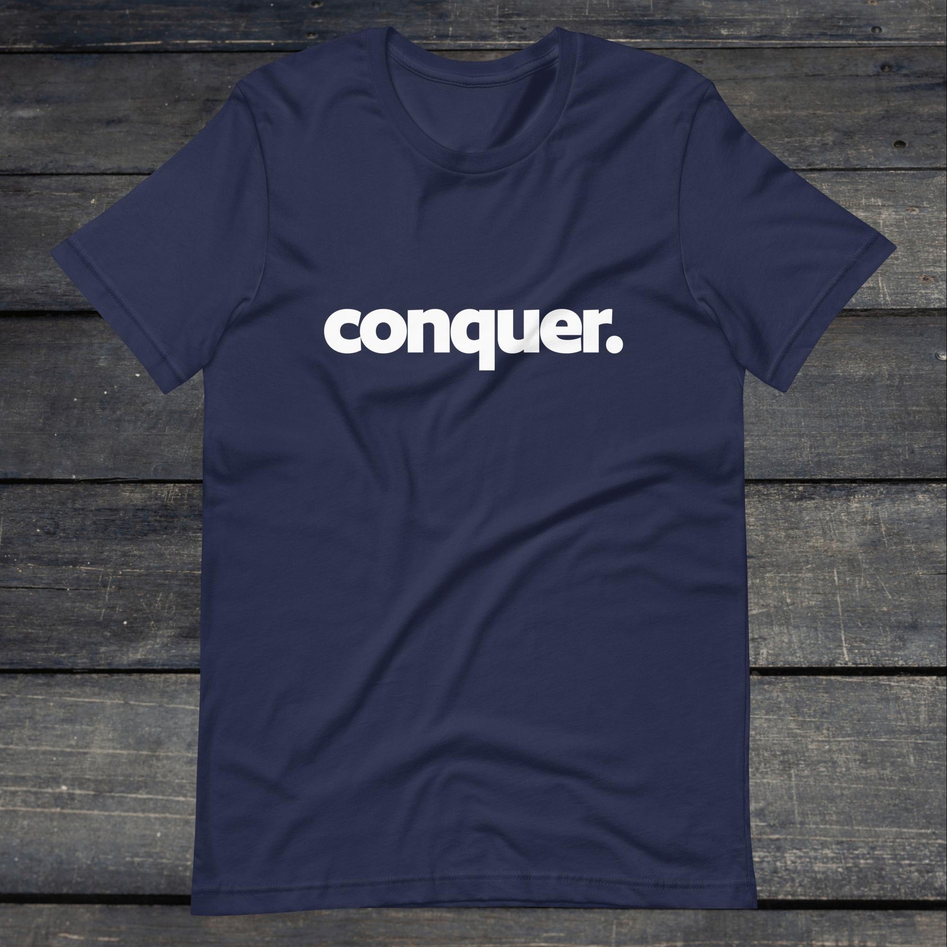 A photo of the Conquer Tee. This tee is navy blue with white text that reads conquer in large bold lettering.