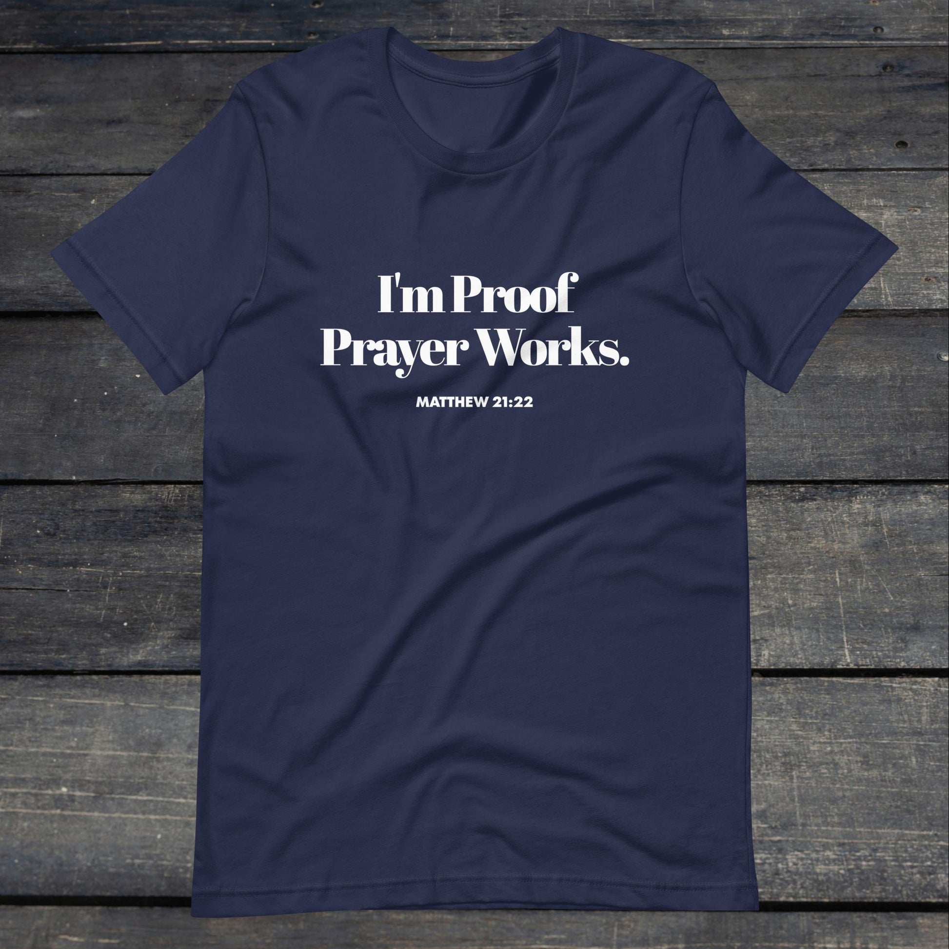 A photo of the "I'm proof prayer works" tee. The shirt color is navy blue with white text that reads "I'm proof prayer works".