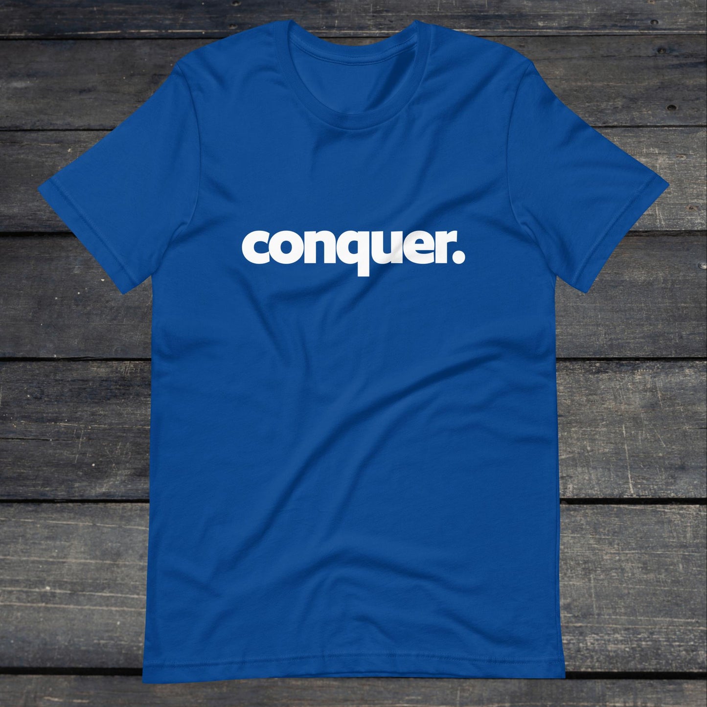 A photo of the Conquer Tee. This tee is royal blue with white text that reads conquer in large bold lettering.