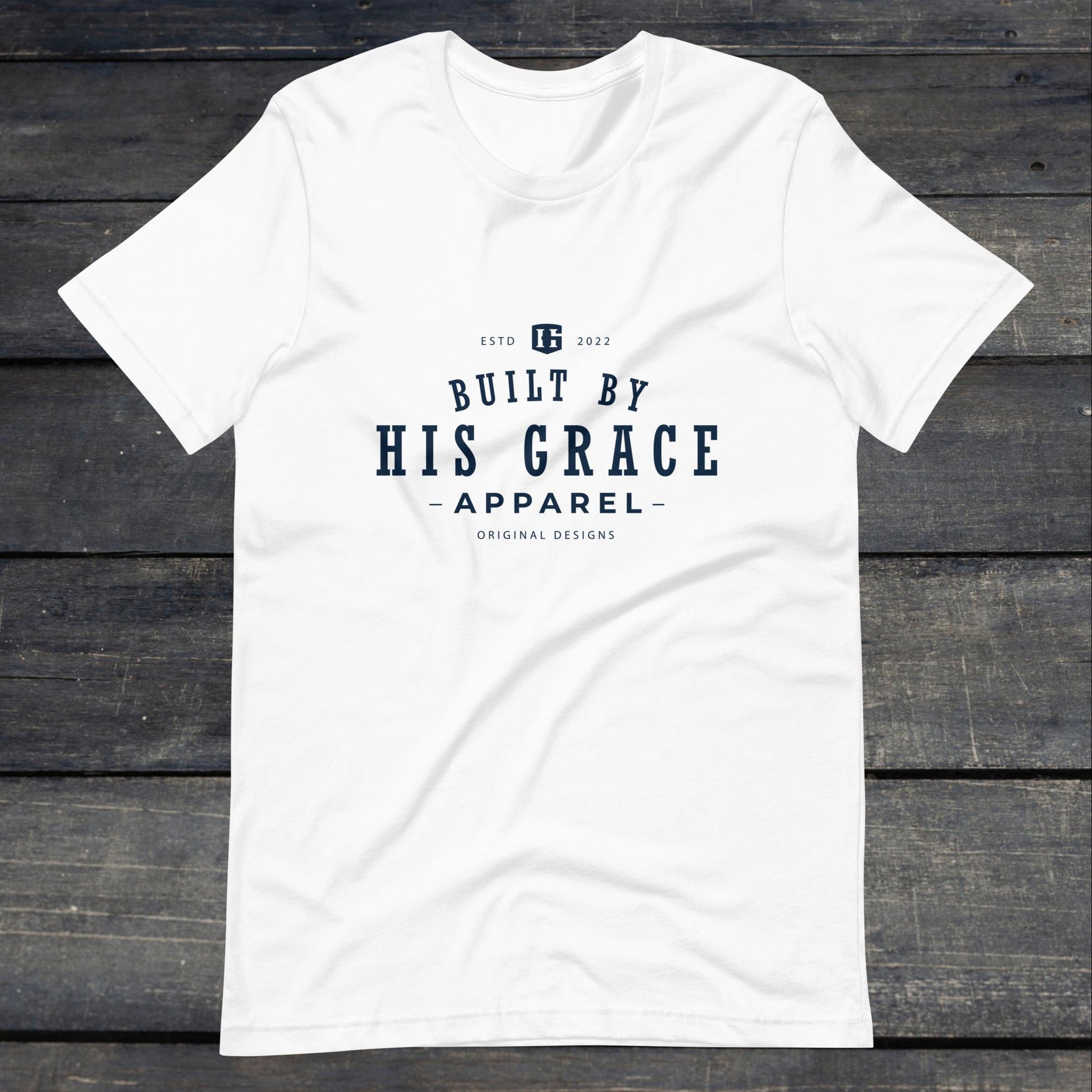 A photo of the "Built By His Grace Apparel" Tee. This tee is white with navy blue text that reads "Built By His Grace Apparel". 